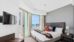 Ein Hotelzimmer mit Bett, Fernseher, Nachttisch mit Lampe und Fenster mit Vorhängen.