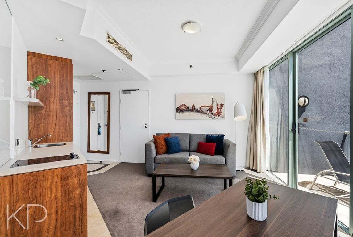 A modern living room with a sofa, coffee table, and a small kitchen area with a sink.
