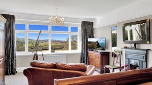 A room with a large window, a television, a fireplace, and a sofa. - Cedar Grange, Old Cleeve (Minehead)