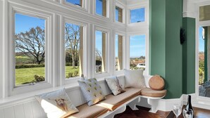 A room with a large window, a bench with cushions, a green accent wall, and a table with a bottle and glass. - Cedar Grange, Old Cleeve (Minehead)