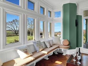 Ein Zimmer mit großem Fenster, einer gepolsterten Bank, einer grünen Akzentwand und einem Tisch mit Flasche und Glas.