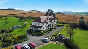 A large house with a driveway, surrounded by green fields and a few parked cars. - Cedar Grange, Old Cleeve (Minehead)