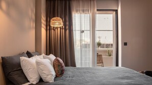A bedroom with a large bed, a hanging light fixture, a view through a window to an outdoor balcony. - Cook's Club City Beach Rhodes (Rhodes)