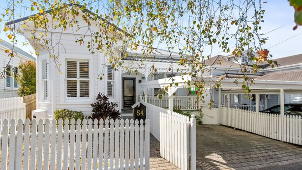 A white residential building with a picket fence, a mailbox, and a number '54' on the door. - Perfection in Ponsonby l by Furnished Rentals (Auckland)