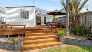 A white house with a wooden deck, outdoor furniture, and a stone wall. - Perfection in Ponsonby l by Furnished Rentals (Auckland)