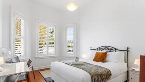 A bedroom with a bed, a desk, a chair, and two windows with blinds. - Perfection in Ponsonby l by Furnished Rentals (Auckland)