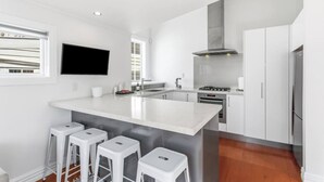 A modern kitchen with a large island, bar stools, a flat-screen TV, and built-in appliances. - Perfection in Ponsonby l by Furnished Rentals (Auckland)