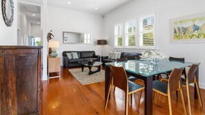 A spacious living area with a glass dining table, black leather sofa, and a wooden floor. - Perfection in Ponsonby l by Furnished Rentals (Auckland)