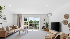 Una sala de estar moderna con un sofá, una mesa de centro, televisor y un balcón con mobiliario exterior.