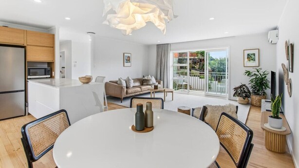 Una cocina moderna con microondas integrado, un comedor con mesa redonda y sillas, un sofá y un balcón con plantas.