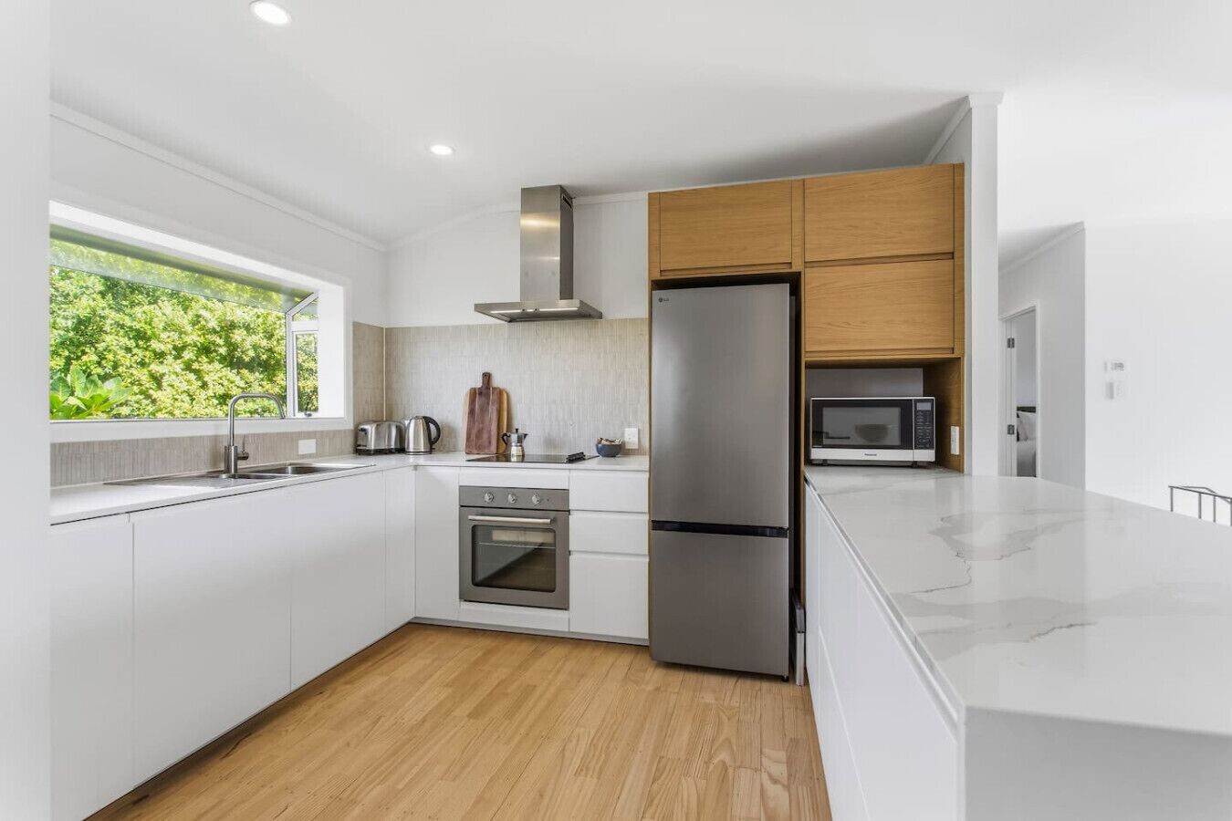 A modern kitchen with white cabinets, a stainless steel refrigerator, a microwave, and a wooden countertop.