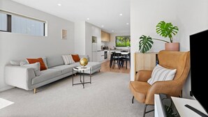 Una sala de estar moderna con sofá, sillón y mesa de centro, una cocina al fondo y un amplio ventanal.