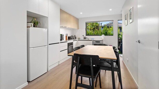 Una cocina moderna con armarios blancos, una mesa de comedor de madera y sillas negras.