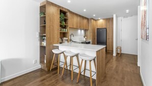 Eine moderne Küche mit Holzschränken, einer weißen Arbeitsplatte und Barhocker.