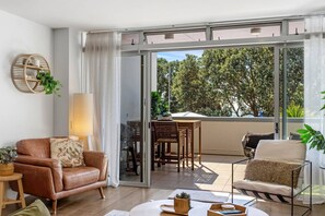 A modern living room with a leather sofa, a coffee table, and a dining area with a table and chairs. - Beach Front Bliss - by Furnished Rentals (Auckland)