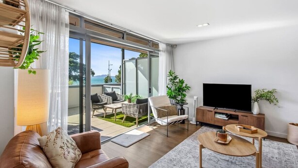 Ein modernes Wohnzimmer mit einer Couch, einem Couchtisch, einem Fernseher und einem Balkon mit Gartenmöbeln.