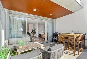 An outdoor patio with wicker furniture, a wooden table, and a dining set. - Beach Front Bliss - by Furnished Rentals (Auckland)