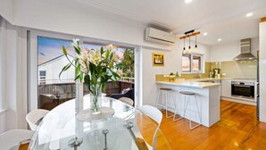 Una cocina moderna con una isla central, una zona de comedor con mesa de vidrio y vistas al exterior.