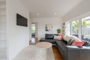 Ein modernes Wohnzimmer mit einem grauen Sofa, einem runden Couchtisch und einem großen Fenster mit Blick auf Grünflächen.