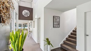 Un intérieur moderne avec un escalier, un panneau mural affichant des phrases motivantes, et une vue à travers une porte vitrée.