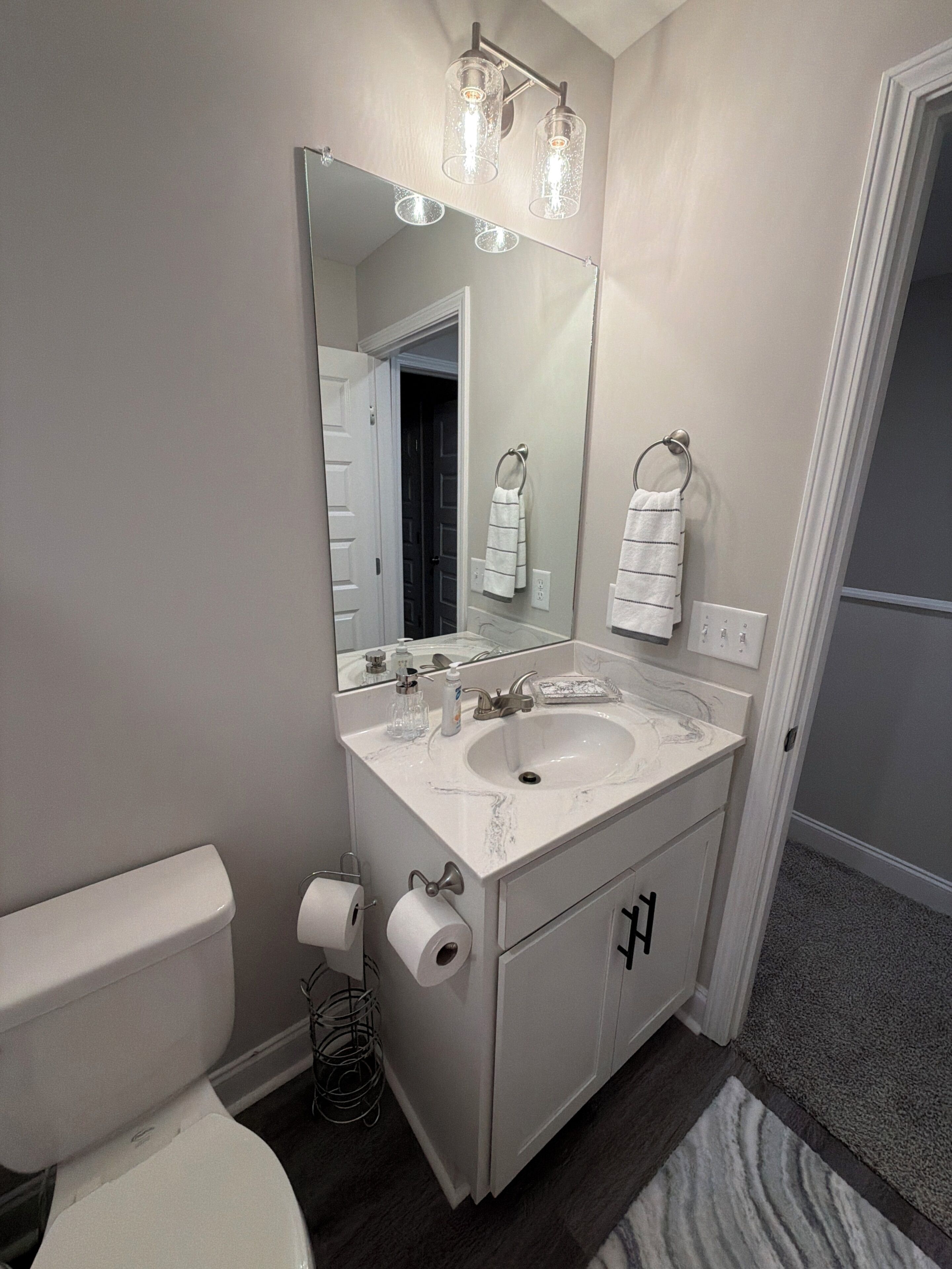 A bathroom with a white sink, mirror, and toilet. There are two towel rings on the wall.