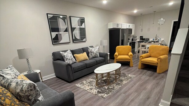 Un salon moderne avec un canapé, des fauteuils, une table basse et un coin cuisine à l’arrière-plan.