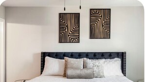 Un lit doté d’une tête de lit capitonnée, de plusieurs oreillers et d’une couvre-lit à motifs.