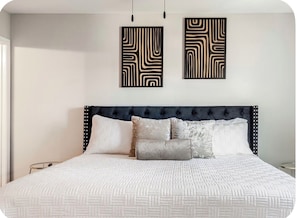 Un lit doté d’une tête de lit capitonnée, de plusieurs oreillers et d’une couvre-lit à motifs.