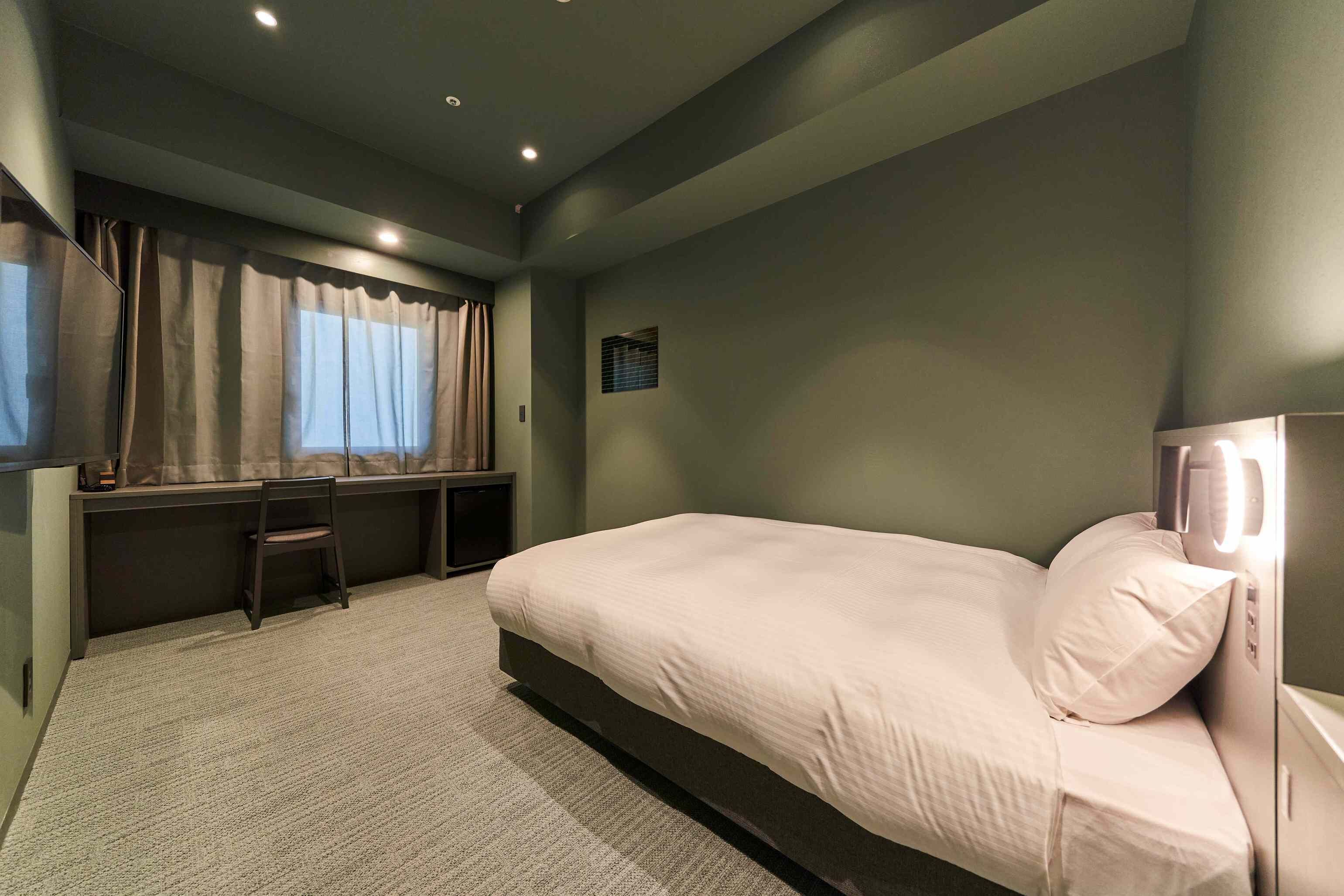 Um quarto com cama, cadeira, escrivaninha e janela com cortinas.