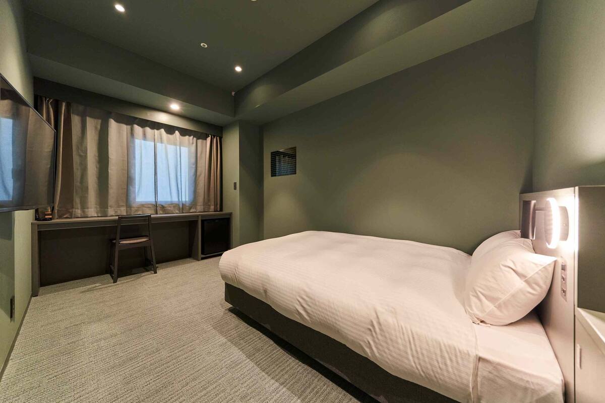Une chambre à coucher avec un lit, une chaise, un bureau et une fenêtre avec des rideaux.