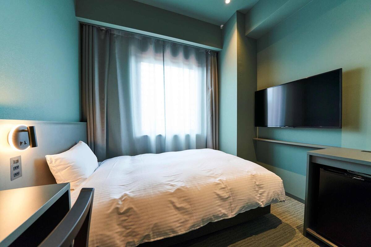 Une chambre d’hôtel avec un lit, une télévision, un bureau et une fenêtre avec des rideaux.