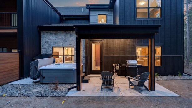 A modern house with a stone facade, a patio with outdoor seating, and a visible kitchen area.