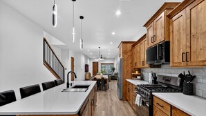 A modern kitchen with wooden cabinets, a central island, stainless steel appliances, and pendant lighting.