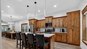 A modern kitchen with wooden cabinets, a central island with bar stools, stainless steel appliances, and pendant lighting.