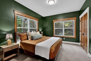 A bedroom with a large bed, two windows, a nightstand, and a door.