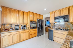 A kitchen with wooden cabinets, a stainless steel refrigerator, a microwave, and a coffee maker. - Strand N Sea • Beach • Hot Tub • Pet Friendly • Channel Islands Harbor (Oxnard)
