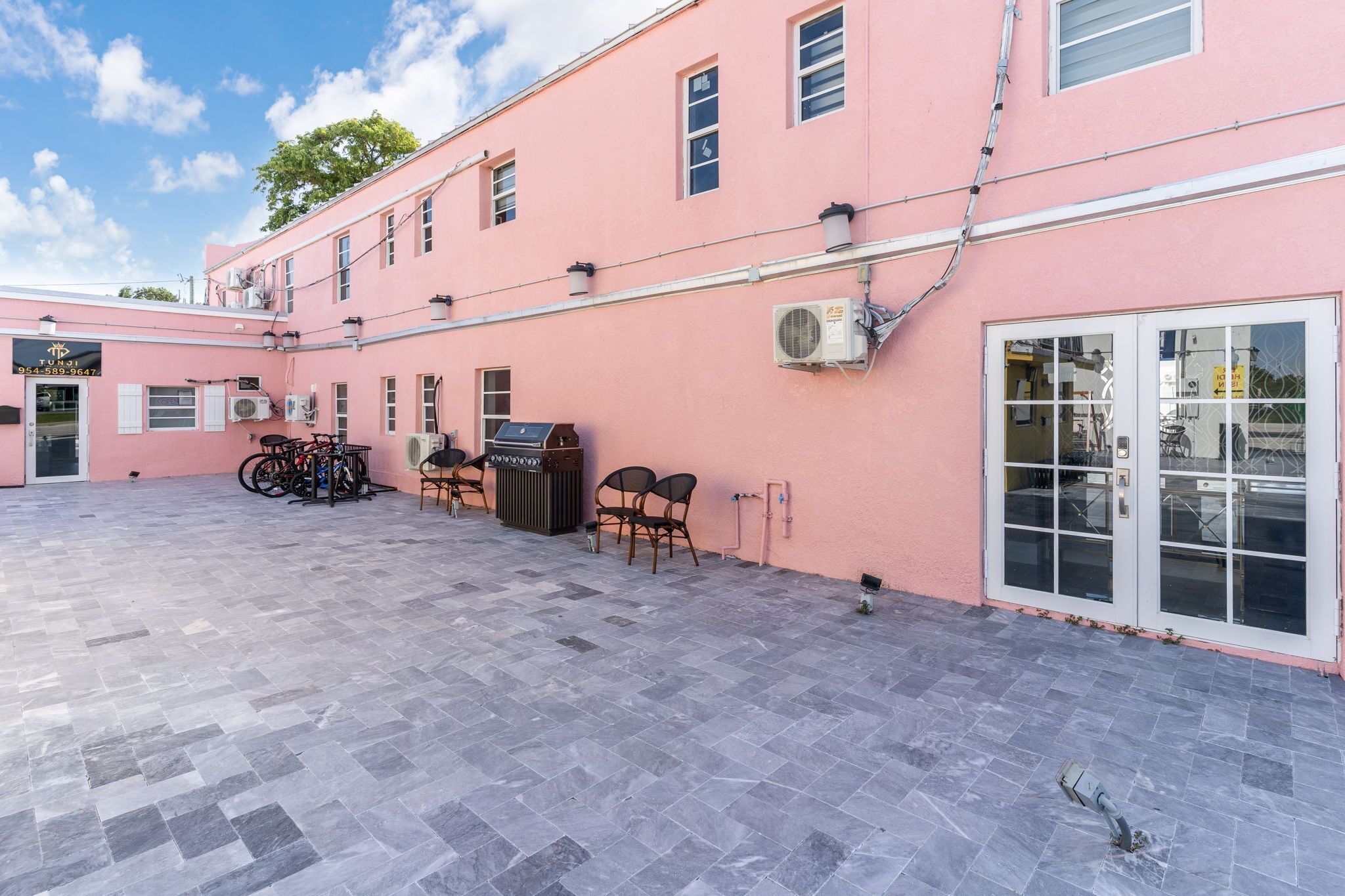 A pink building with a tiled patio, a grill, and outdoor seating.