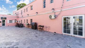 A pink building with a tiled patio, a grill, and outdoor seating.