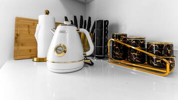 Une bouilloire blanche, une machine à café et un plateau avec des tasses noires et dorées, le tout posé sur un plan de travail blanc.