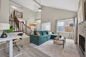 A spacious living area with a staircase, a green sofa, a dining table, and a fireplace. - Beautiful 3 bedroom home in peaceful Spring / Cypress area near downtown Houston (Houston)