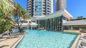 A swimming pool with lounge chairs, surrounded by tall buildings and palm trees.