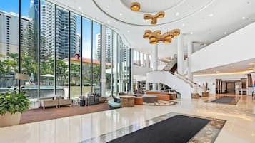 A spacious lobby with a central staircase, seating areas, and large windows offering views of the surrounding buildings.