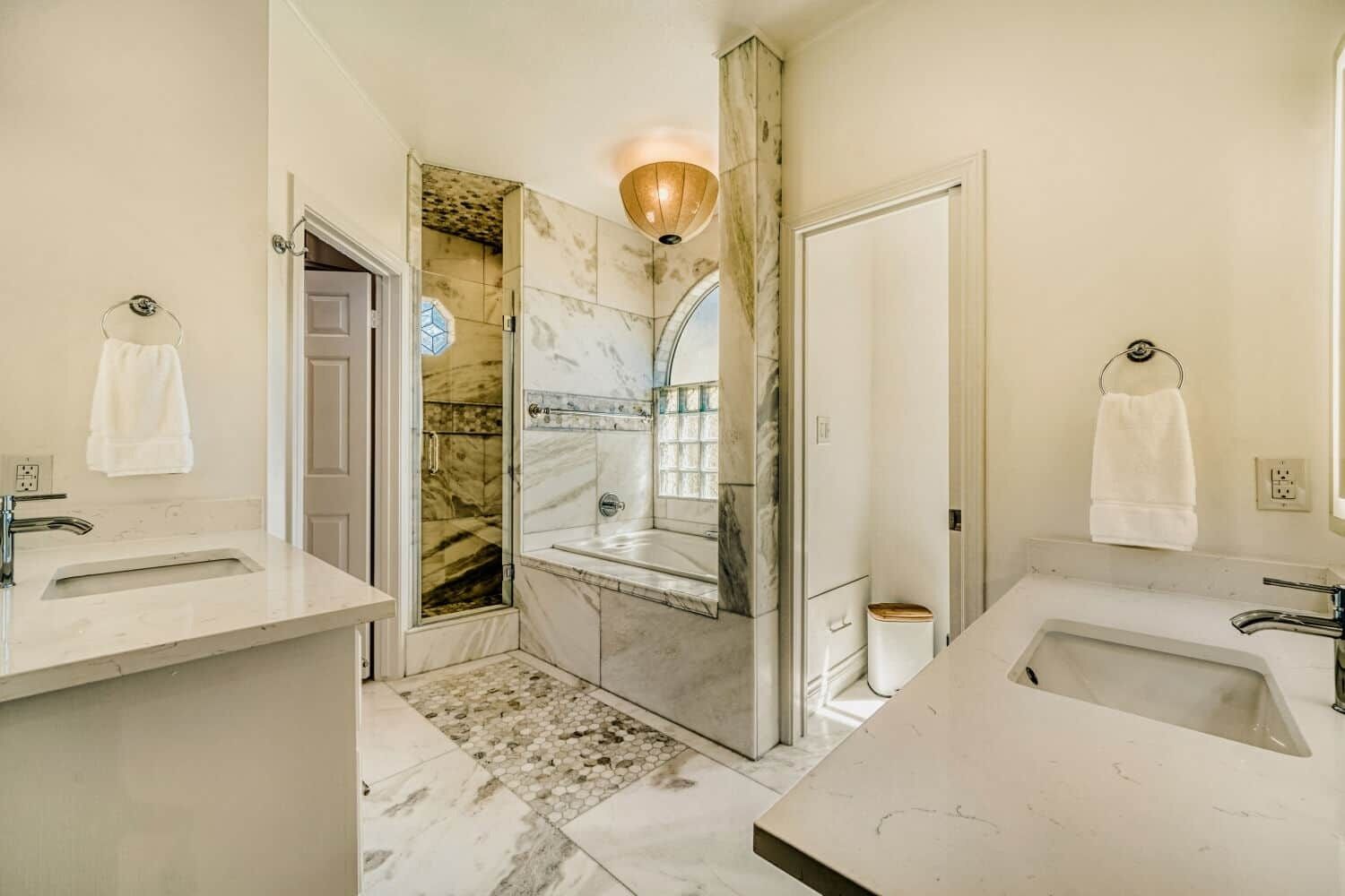 Un bagno moderno con due lavabi, una doccia e un box doccia rivestito in marmo.