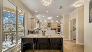A modern kitchen with a large island, bar seating, and a view through large windows. - LuxuryLake Austin Retreat: Game Room + Fire Pit, Minutes to Downtown (Austin)