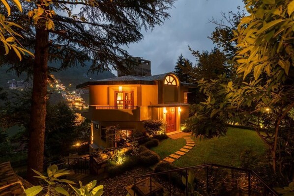 Ein zweistöckiges Haus mit Balkon, gut beleuchtetem Eingang und Garten mit einem Kiesweg.
