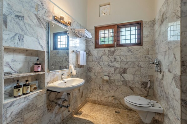 Une salle de bain avec un mur en marbre, un lavabo, des toilettes, une fenêtre et des étagères contenant des articles de toilette.