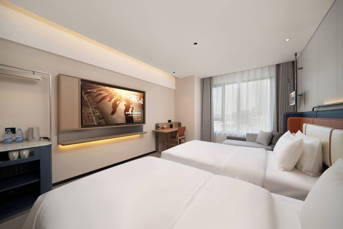 A hotel room with two beds, a desk, a TV, and a large window.