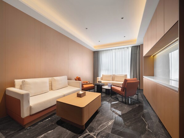 Ein modernes Hotelzimmer mit Sofa, Ohrensessel, Couchtisch und Blick auf die Stadt.