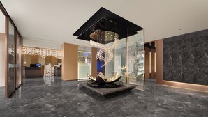 Un vestíbulo moderno con una instalación artística central, un mostrador de recepción y un suelo de mármol.