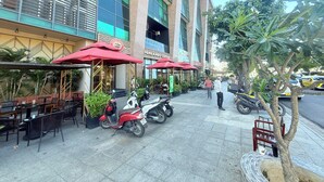Un café avec une terrasse, des parasols rouges et une rangée de scooters garés.
